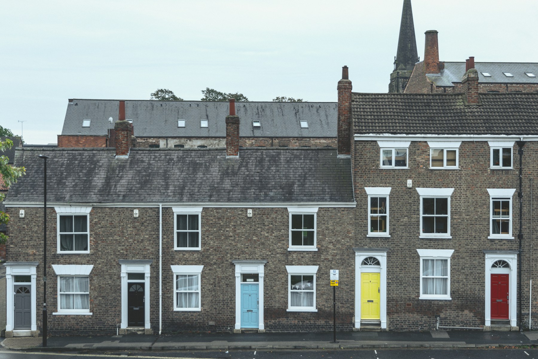 Row of London terraced houses with characterful coloured front doors and slate roofs under a cool overcast sky